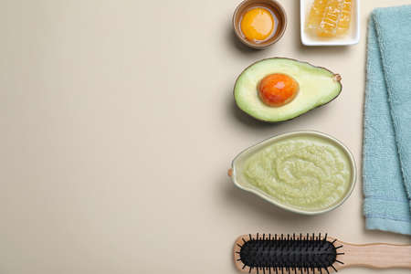 Homemade hair mask in bowl, ingredients, towel and wooden brush on beige background, flat lay. Space...