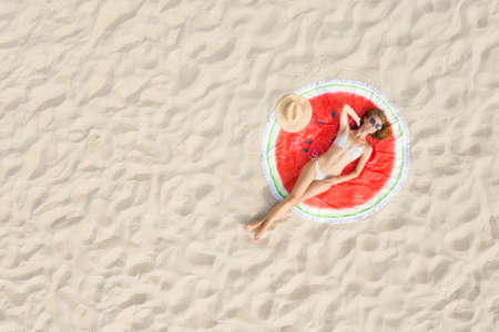 Woman sunbathing on round beach towel at sandy coast, aerial view. Space for textの写真素材