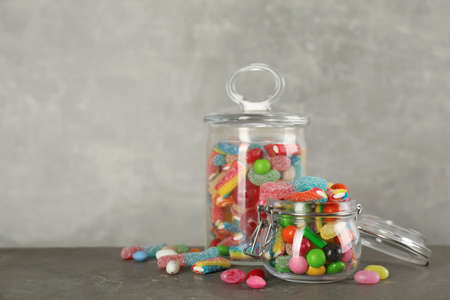 Jars with different delicious candies on gray table, space for textの写真素材