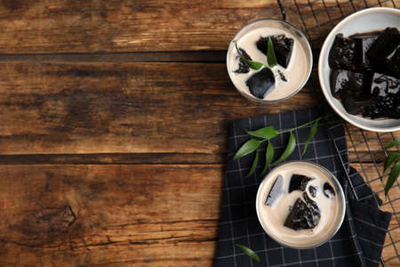 Glasses of milk with grass jelly on wooden table, flat lay. Space for text