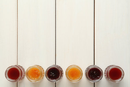 Jars of different jams on white wooden table, flat lay. Space for textの写真素材