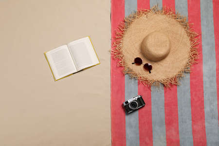 Beach towel, hat, sunglasses, camera and open book on sand, flat layの写真素材