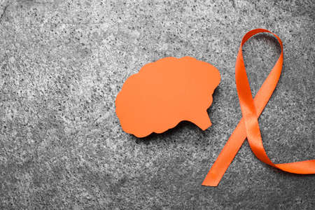 Orange ribbon and paper brain cutout on gray table, flat lay with space for text. Multiple sclerosis awarenessの写真素材