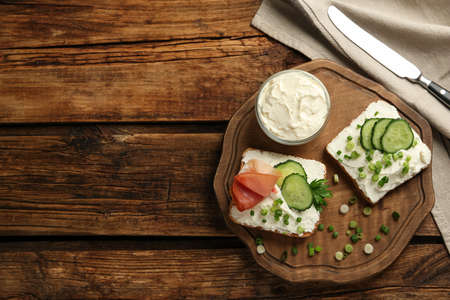 Delicious sandwiches with cream cheese and other ingredients on wooden table, flat lay. Space for...
