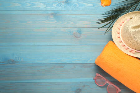Beach towel, sunglasses and hat on light blue wooden background, flat lay. Space for textの写真素材
