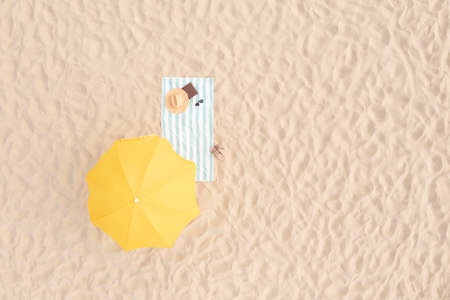 Beach umbrella near towel and other vacationist's stuff on sand, aerial view. Space for textの写真素材