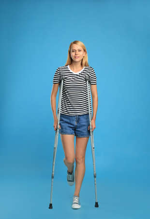 Young woman with axillary crutches on light blue backgroundの写真素材