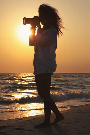 Photographer taking photo of sea with professional camera at sunsetの写真素材