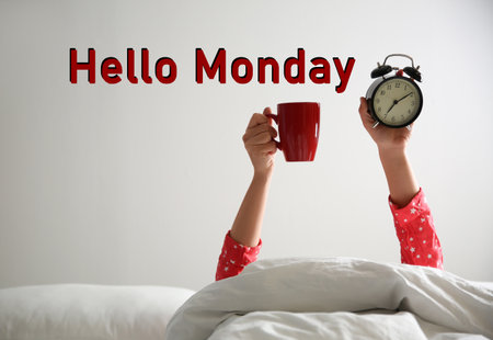 Hello Monday, start your week with good mood. Closeup view of woman with cup and alarm clock lying in bedの写真素材