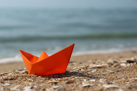 Orange paper boat on sandy beach near sea, space for text