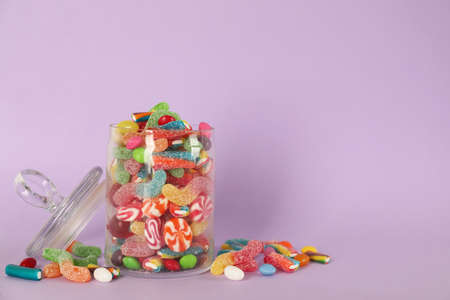 Jar with different delicious candies on violet background, space for textの写真素材