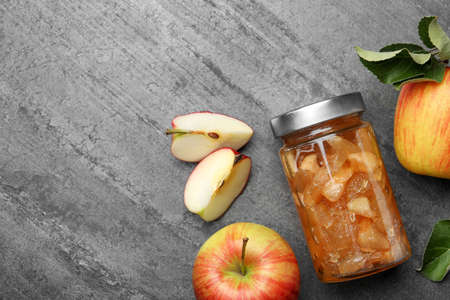 Tasty apple jam in glass jar and fresh fruits on gray table, flat lay. Space for textの写真素材