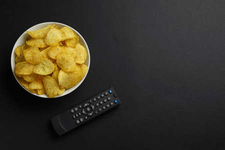 Modern tv remote control and chips on black background, flat lay. Space for textの写真素材