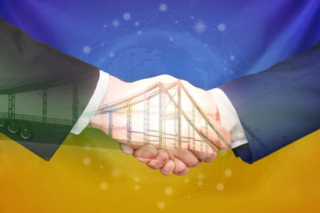 Double exposure of bridge and men shaking hands against Ukrainian national flag, closeup. International relationshipsの写真素材