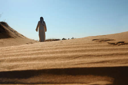 Man in arabic clothes walking through desert on sunny day, back viewの写真素材