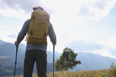 Tourist with backpack and trekking poles enjoying mountain landscape, back view. Space for textの写真素材