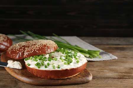 Delicious bagel with cream cheese and green onion on wooden tableの写真素材