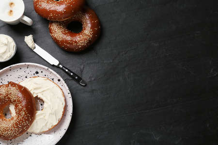 Delicious bagel with cream cheese and coffee on black table, flat lay. Space for textの写真素材