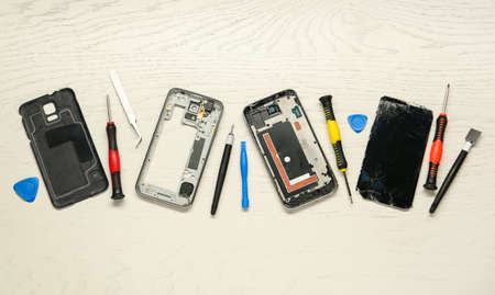 Parts of damaged smartphone and repair tool set on light beige wooden table, flat lay