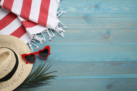 Beach towel, heart shaped sunglasses and straw hat on light blue wooden background, flat lay. Space for textの写真素材
