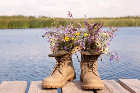 Boots with beautiful wild flowers on wooden pier near lakeの写真素材
