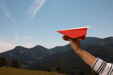 Woman with red paper plane in mountains on sunny day, closeup. Space for textの写真素材