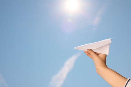 Woman holding paper plane against blue sky, closeup. Space for textの写真素材