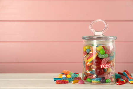 Jar with different delicious candies on white wooden table against pink background, space for textの写真素材