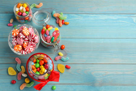 Jars with different delicious candies on light blue wooden table, flat lay. Space for textの写真素材
