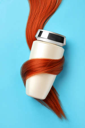 Bottle wrapped in lock of hair on light blue background, top view. Natural cosmetic productの写真素材