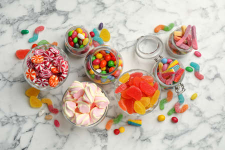 Jars with different delicious candies on white marble table, flat layの写真素材