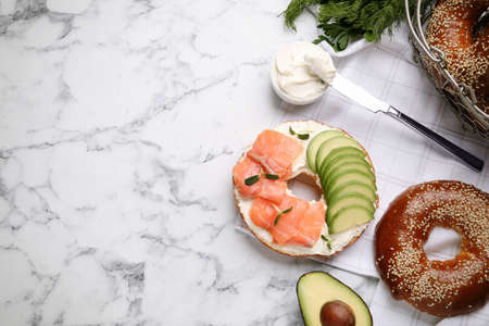 Delicious bagel with cream cheese, salmon and avocado on white marble table, flat lay. Space for textの写真素材