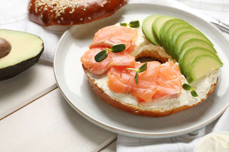 Delicious bagel with cream cheese, salmon and avocado on white wooden table, closeupの写真素材