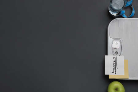 Flat lay composition with word Anorexia and scales on dark gray background. Space for textの写真素材
