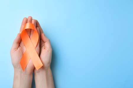Man holding orange ribbon on light blue background, top view with space for text. Multiple sclerosis awarenessの写真素材