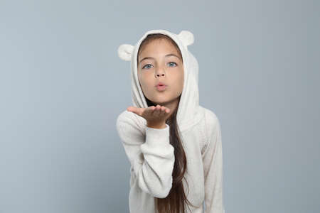 Cute girl in adorable white pajamas blowing kiss on light gray backgroundの写真素材