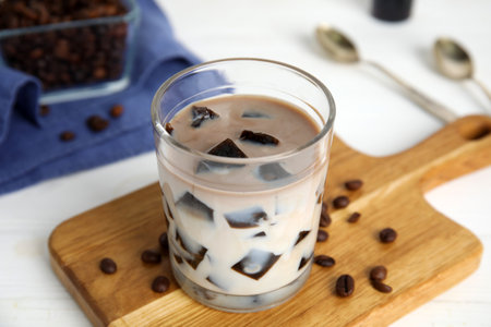 Glass of milk with grass jelly and coffee beans on white table, closeup