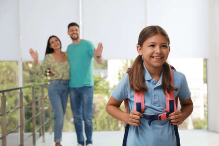 Parents waving goodbye to their daughter in schoolの写真素材