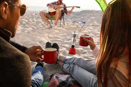 Friends resting on sandy beach. View from camping tent