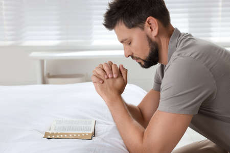 Religious man with Bible praying in bedroomの写真素材