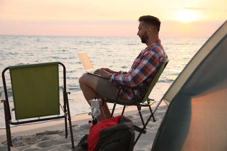 Man using laptop in camping chair on sandy beachの写真素材