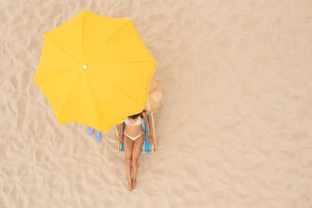 Woman resting in sunbed under yellow beach umbrella at sandy coast, aerial view. Space for textの写真素材