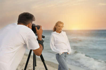 Photographer taking picture of model with professional camera near sea