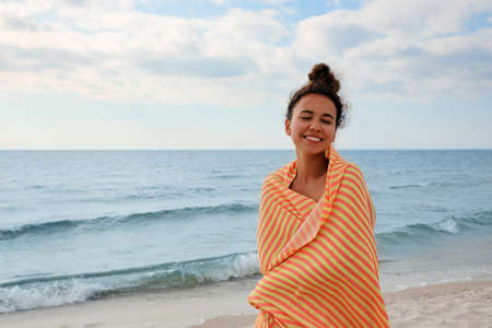 Beautiful African American woman with beach towel on seashoreの写真素材