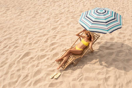 Woman resting in sunbed under striped beach umbrella at sandy coast, space for textの写真素材