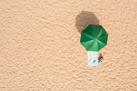 Beach umbrella near towel and other vacationist's stuff on sand, aerial view. Space for textの写真素材