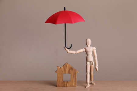 Mannequin holding small umbrella over house figure on wooden tableの写真素材