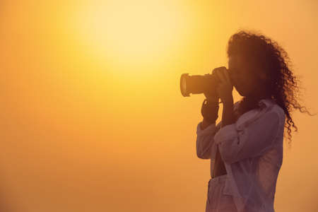 Photographer taking photo with professional camera outdoors at sunsetの写真素材