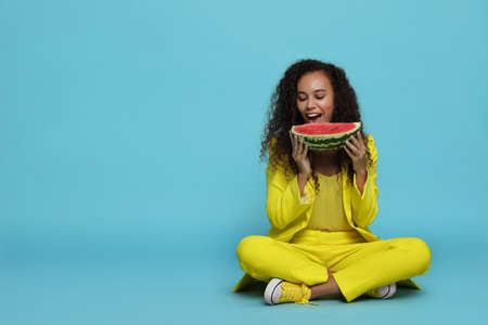Beautiful young African American woman with watermelon on light blue background. Space for textの写真素材