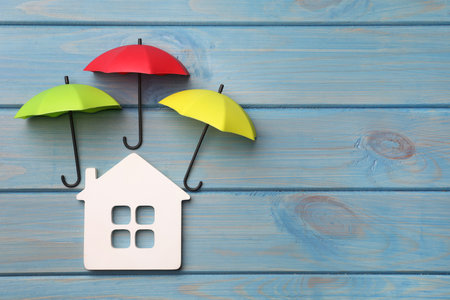 Small umbrellas and house figure on light blue wooden background, flat lay. Space for textの写真素材